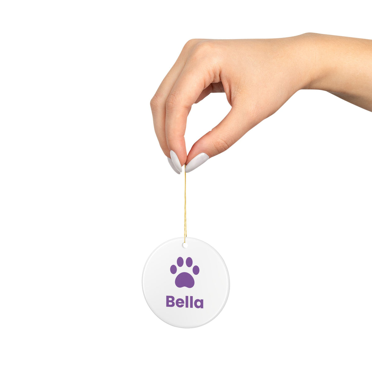 Hand holding a round ceramic dog ornament with a purple paw print and the name Bella